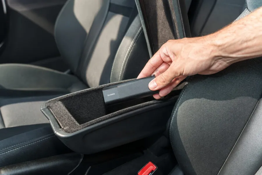 Hand slipping a GPS Tracker Pro Max into a storage tray beside a car seat