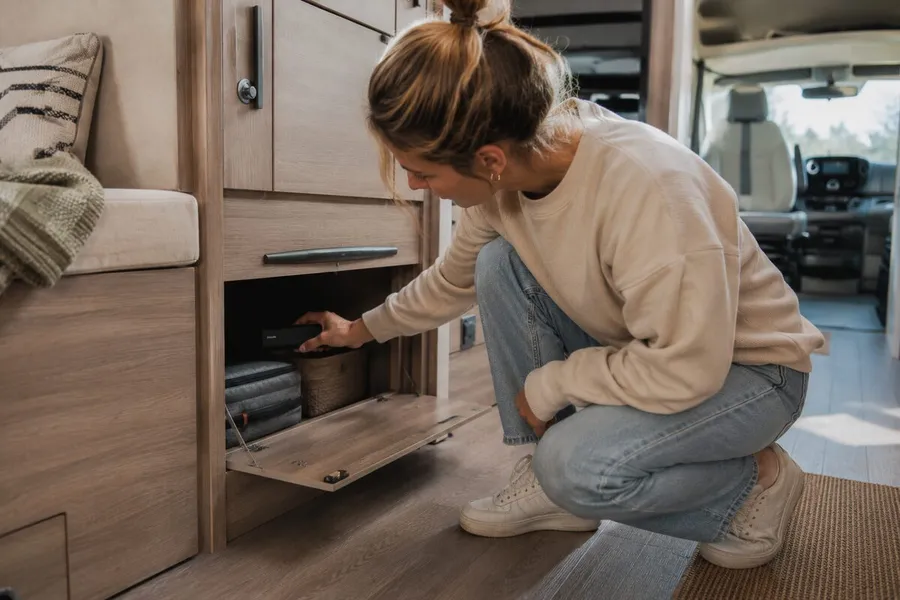 Woman hiding a GPS Tracker Pro Max in a storage compartment inside a camper van