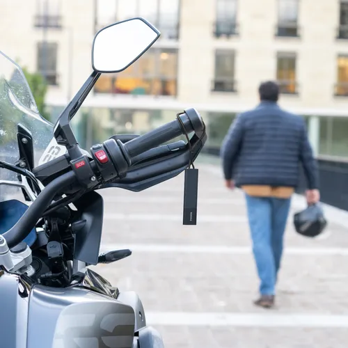 a Tracker GPS Pro hanging on a motorcycle handlebar with a man in the background