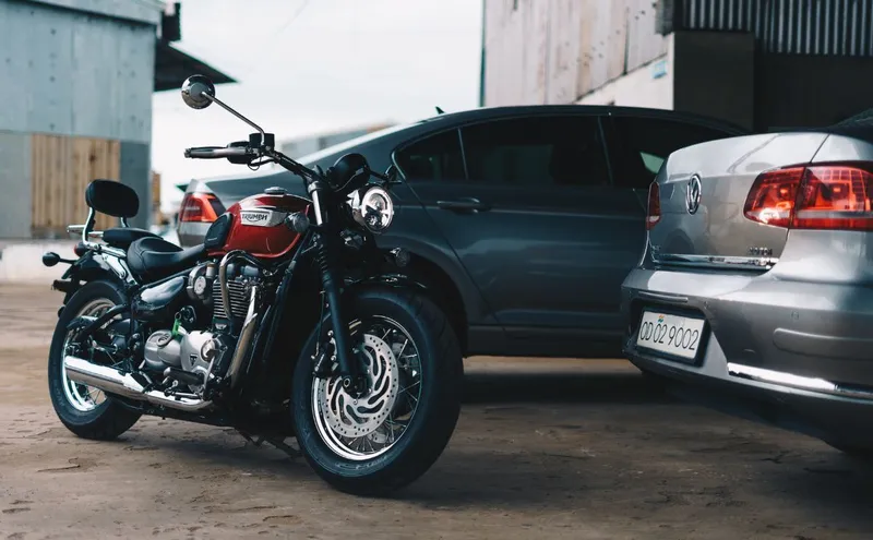 A courtyard with a vintage motorcycle and 2 cars.