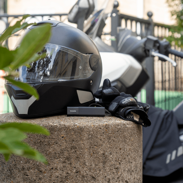 Invoxia GPS tracker placed next to a motorbike helmet, in front of a scooter